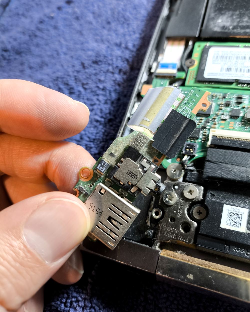 Manos de un técnico retirando la placa de puertos de una laptop